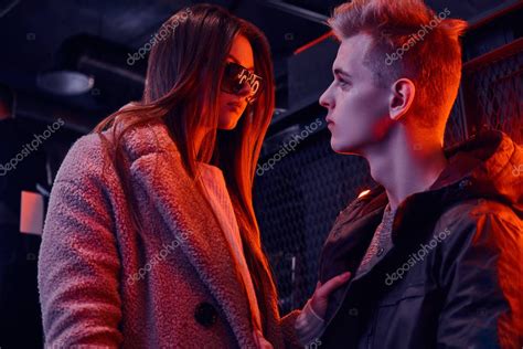 Una pareja joven besándose apasionadamente en un salón oscuro.